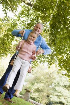 Royalty Free Photo of a Grandfather Pushing a Granddaughter on a Swing