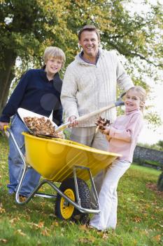 Father and children outdoors shoveling leaves into wheelbarrow and smiling (selective focus)