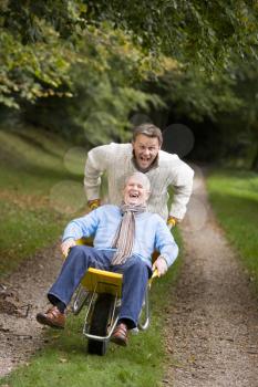 Royalty Free Photo of a Man Pushing Another Man in a Wheelbarrow