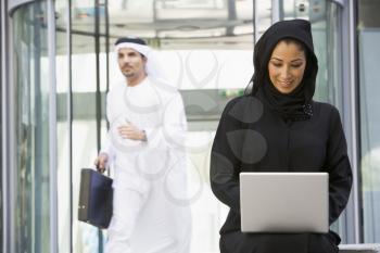 Royalty Free Photo of a Woman With a Laptop and a Man Walking Behind Her