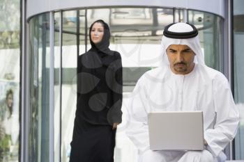 Royalty Free Photo of a Man With a Laptop and a Woman Walking Behind