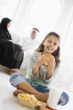 Royalty Free Photo of a Child Eating Fast Food With Her Parents Behind Her