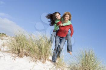 Royalty Free Photo of a Girl Giving a Girl a Piggyback Ride on Sand