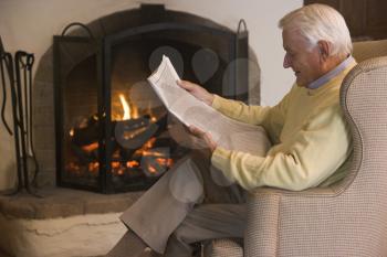 Royalty Free Photo of a Man Reading a Paper by the Fireplace