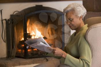 Royalty Free Photo of a Woman Reading a Newspaper by a Fireplace