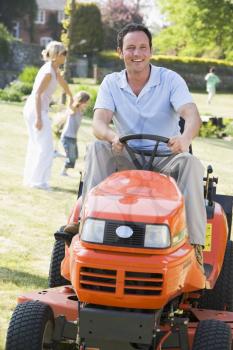 Royalty Free Photo of a Man On a Riding Lawn Mower With His Wive and Child in the Background