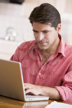 Royalty Free Photo of a Man Using a Laptop at a Kitchen Table