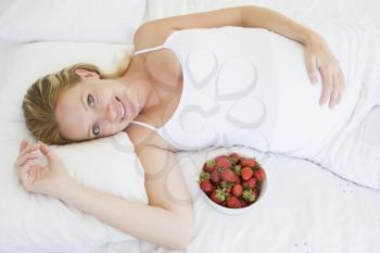 Royalty Free Photo of a Pregnant Woman Eating Strawberries in Bed