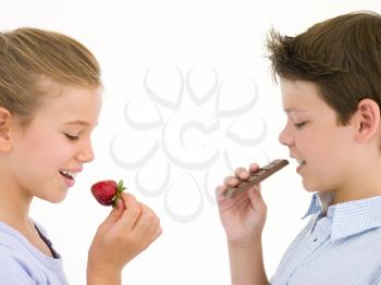 Royalty Free Photo of a Girl Eating a Strawberry and a Boy Eating a Chocolate Bar