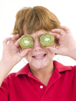 Royalty Free Photo of a Young Boy Holding Kiwi Halves Over His Eyes