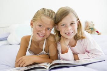 Royalty Free Photo of Two Girls Lying on a Bed Reading a Book