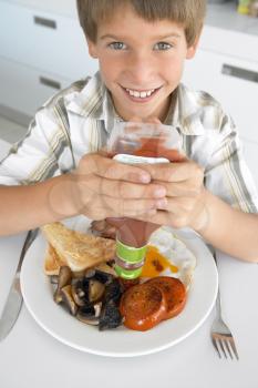 Royalty Free Photo of a Boy Eating Bacon and Eggs With Ketchup