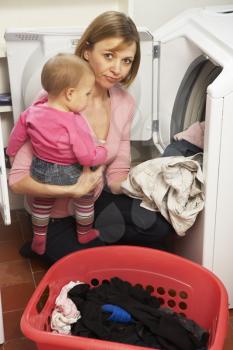 Royalty Free Photo of a Woman Doing Laundry and Holding a Baby