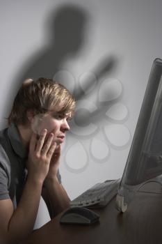 Royalty Free Photo of a Boy Frightening at the Computer With a Menacing Shadow Behind Him