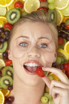 Royalty Free Photo of a Girl Surrounded By Fruit Eating Strawberry