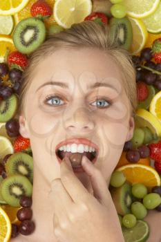 Royalty Free Photo of a Girl Surrounded by Fruit Eating Chocolate