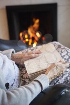 Royalty Free Photo of an Older Woman With a Book by the Fire