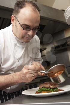Chef Adding Sauce To Dish In Restaurant Kitchen