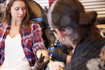 Woman Sitting In Chair Having Tattoo On Arm In Parlor