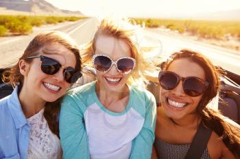 Three Female Friends On Road Trip In Back Of Convertible Car