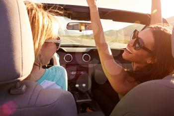 Two Female Friends On Road Trip Driving In Convertible Car