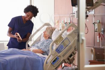 Hospital Nurse With Digital Tablet Talks To Senior Patient