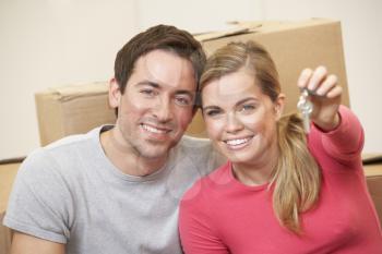 Young couple sit on the floor around boxes holding key in hand