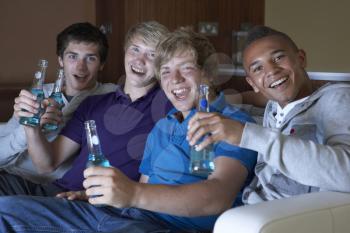 Group Of Teenage Boys Sitting On Sofa At Home Watching Drinking Alcohol