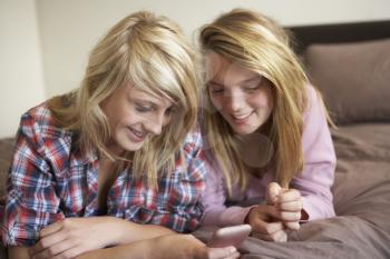 Two Teenage Girls Lying On Bed Looking At Pregnancy Testing Kit