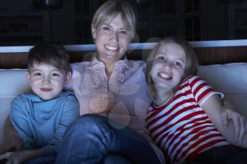 Mother And Children Watching Programme On TV Sitting On Sofa Together