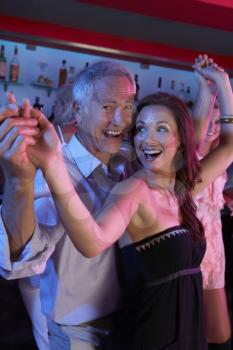Senior Man Dancing With Younger Woman In Busy Bar