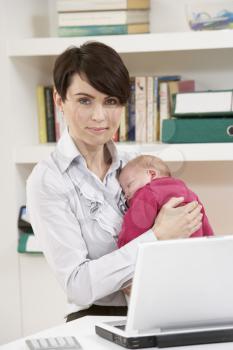 Woman With Newborn Baby Working From Home Using Laptop