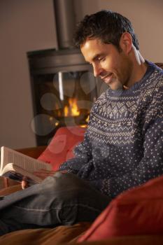 Middle Aged Man Relaxing With Book By Cosy Log Fire