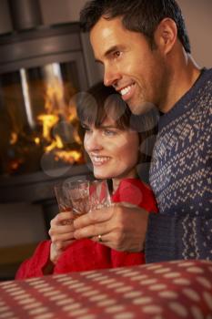 Middle Aged Couple Sitting On Sofa Watching TV By Cosy Log Fire