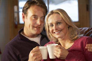 Middle Aged Couple Sitting On Sofa With Hot Drinks