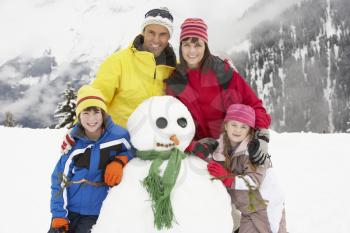 Family Building Snowman On Ski Holiday In Mountains