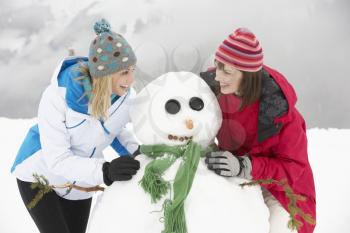 Two Female Friends Building Snowman On Ski Holiday In Mountains