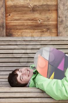 Teenage Boy With Snowboard On Ski Holiday Lying On Wooden Bench