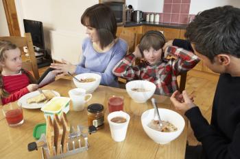 Parents Taking Away Gadgets From Children Whilst Eating Breakfast Together In Kitchen