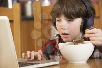 Boy Using Laptop Whilst Eating Breakfast