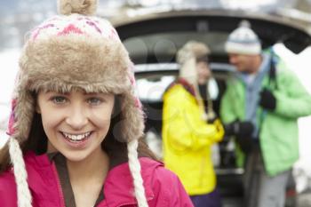 Teenage Girl Smiling At Camera Whilst Family Load Skis In Boot Of Car
