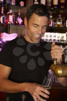 Portrait Of Barman Standing Behind Bar Pouring Beer