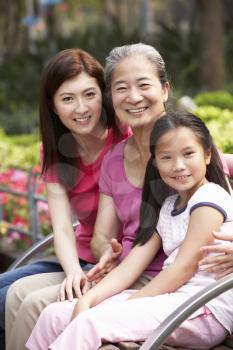 Female Multi Genenration Chinese Family Group Sitting On Bench In Park Together