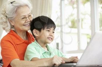 Chinese Grandmother And Grandson Sitting At Desk Using Laptop At Home