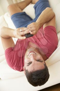 Man Lying Upside Down On Sofa Sending Text Message