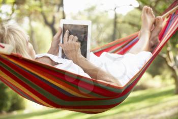 Senior Woman Relaxing In Hammock With  E-Book