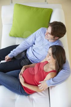 Overhead View Of Man Watching TV On Sofa With Pregnant Wife