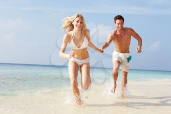 Couple Running Through Waves On Beach Holiday
