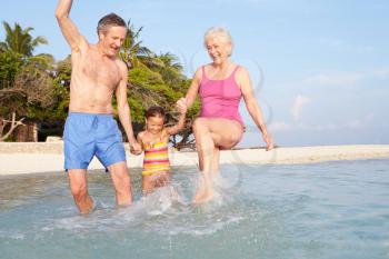 Grandparents With Granddaughter Splashing In Sea On Beach