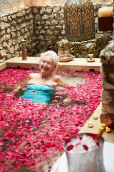 Senior Woman Relaxing In Flower Petal Covered Pool At Spa